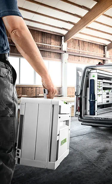 Craftsman unloads Festool tools from a van and takes them to the building site of a modern house.