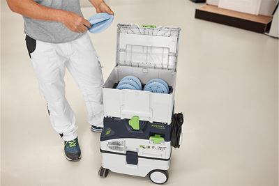 A tradesperson stands next to a Systainer full of abrasives