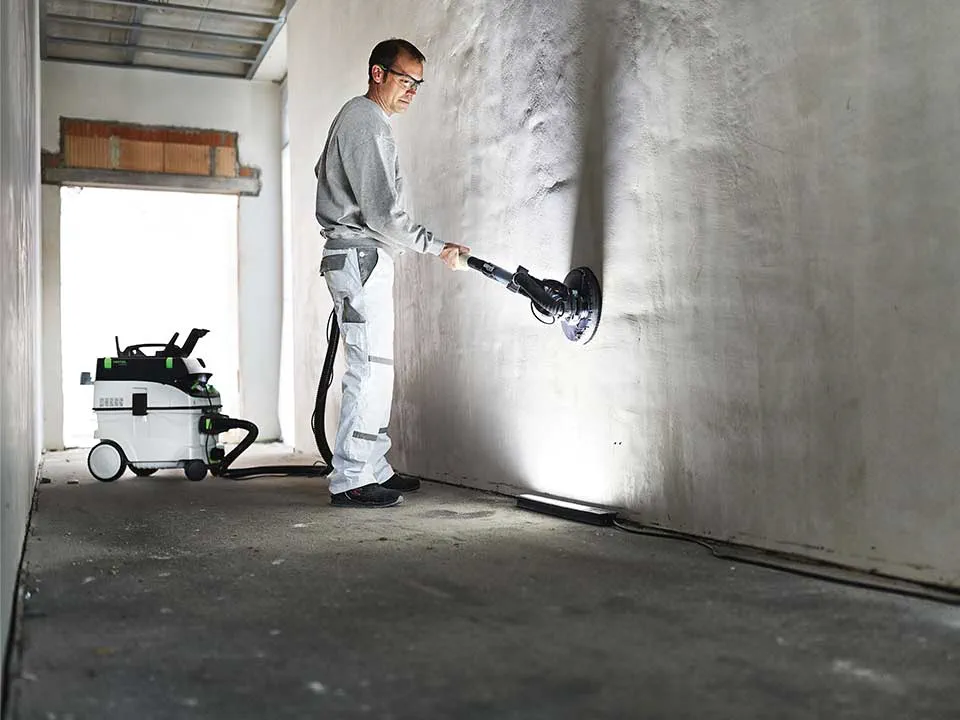 A craftsman illuminates a wall with the help of the painter's Surface control light and sands it down