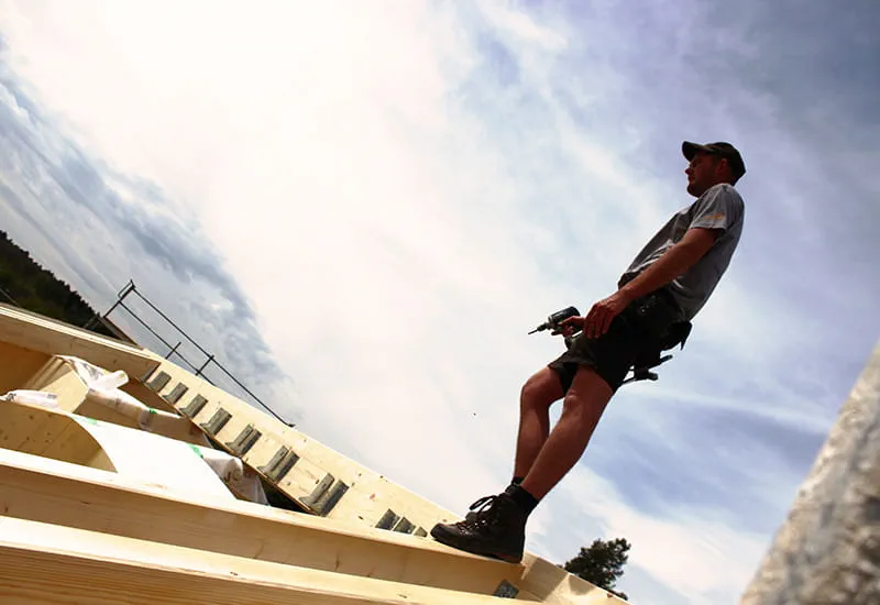 A carpenter with the cordless drill DRC 18/4 from Festool on top of a solid-wood house.