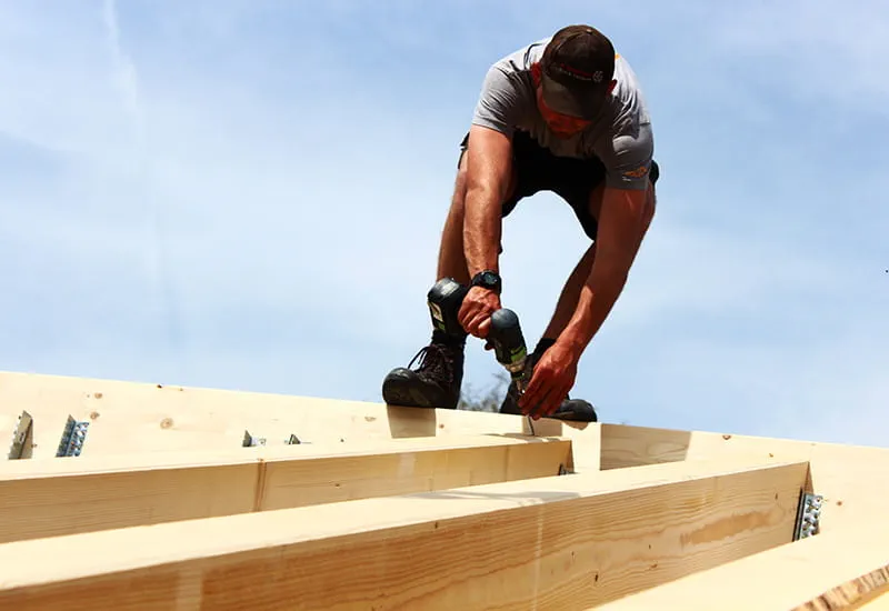 A carpenter with the cordless drill DRC 18/4 from Festool on top of a solid-wood house.